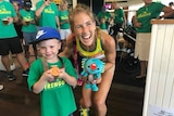 Jess crouches down next to a young boy who is wearing her bronze medal around his neck.