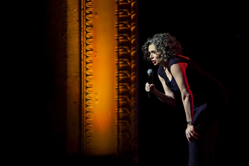 The comedian Judith Lucy on stage with a micrphone being forward and speaking to the audience