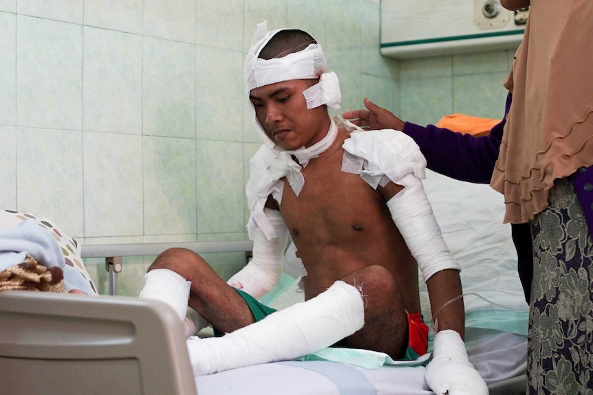 Anggi Aji Pangetsu sits on a hospital bed wrapped in bandages as a woman pats his back