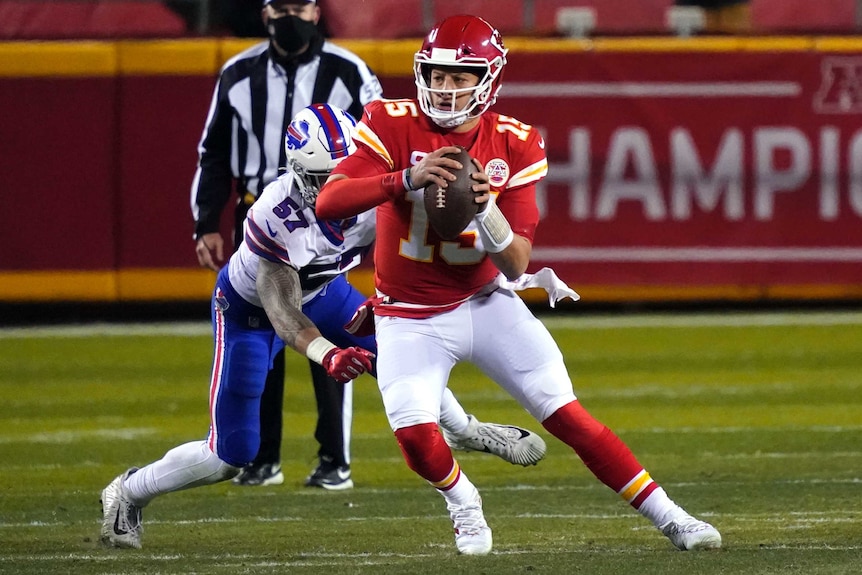 Patrick Mahomes holds an American football in both hands and turns off his straight left leg as a Bills player pursues him