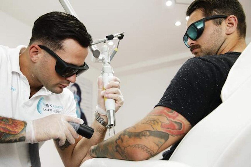 Tattoo removalist performs a treatment on a client inside a clinic. Both are wearing sunglasses