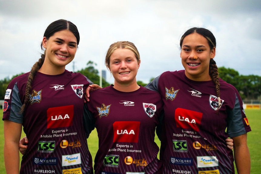 Three young women in football uniforms standing next to each other