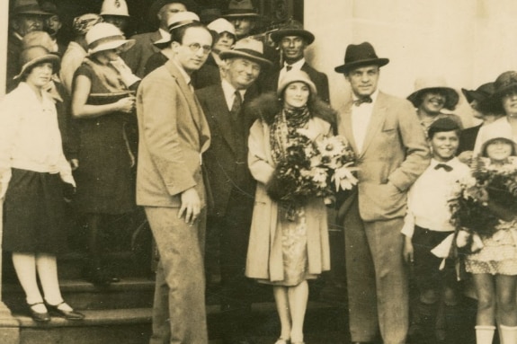 A group of people standing in arch way with one woman holding a bunch of flowers.
