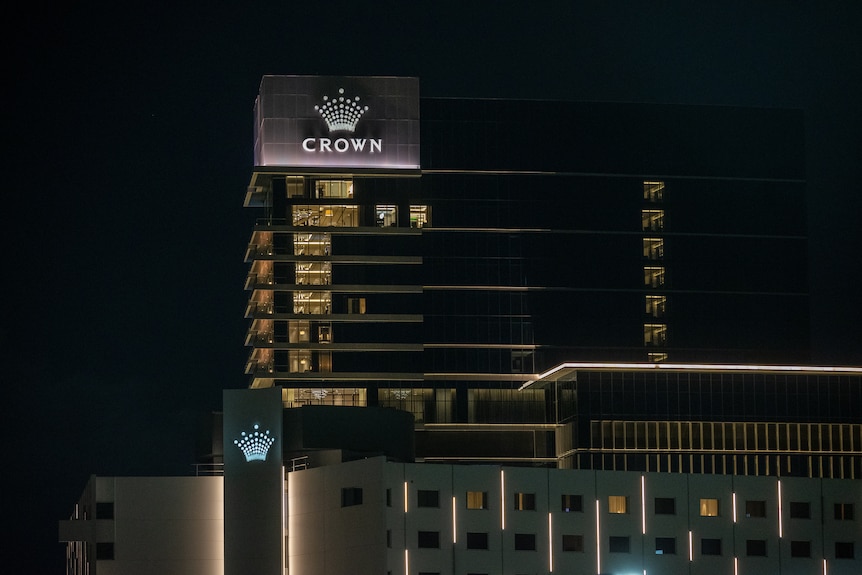 Tall buildings in the dark with lights on with an illuminated sign with the word Crown below a crown symbol.