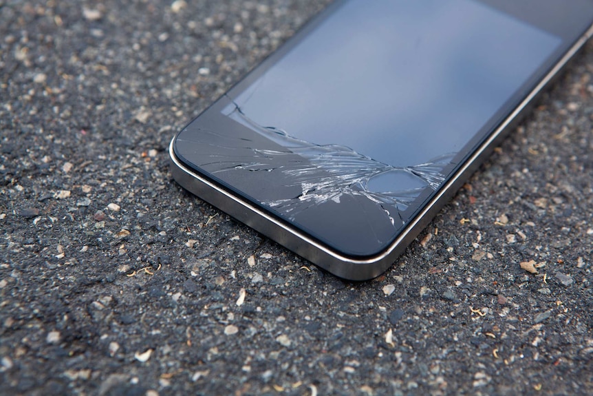 An iPhone lies on the ground with a cracked screen