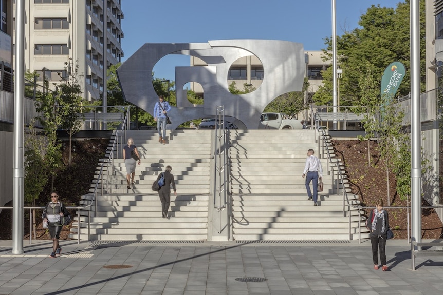 Outdoor staircase in public walkway with a large sculpture at the top of the stairs.