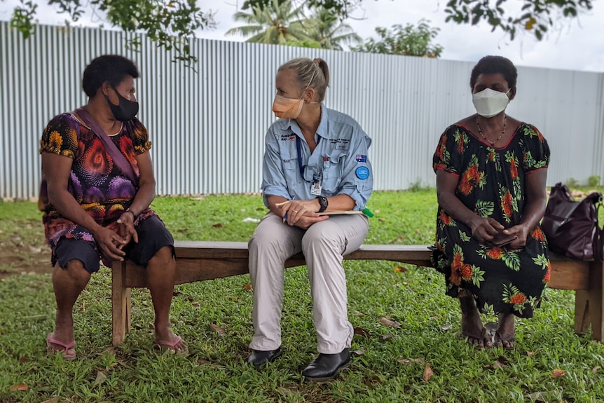 a blonde female doctor wearing a blue shirt talking to a PNG woman