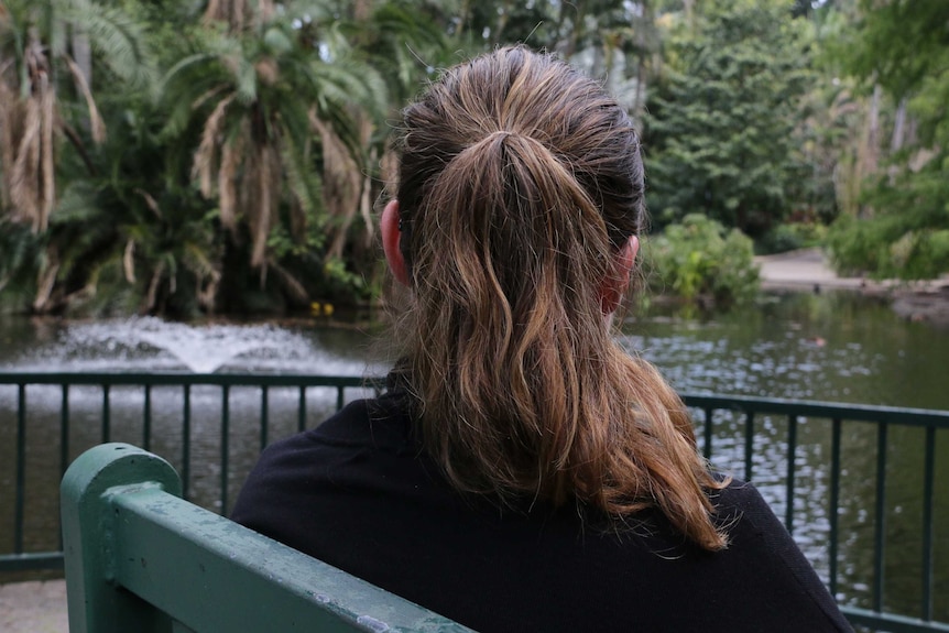 A woman with her hair in a ponytail sits on a bench in a park