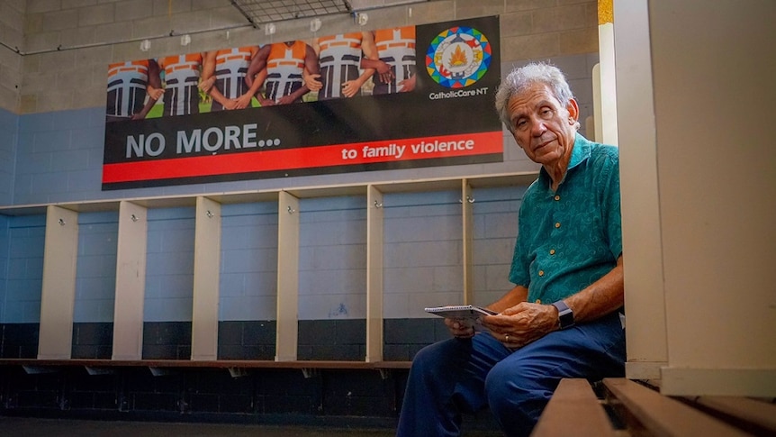 Charlie King sits in the locker room next to a family violence campaign sign.