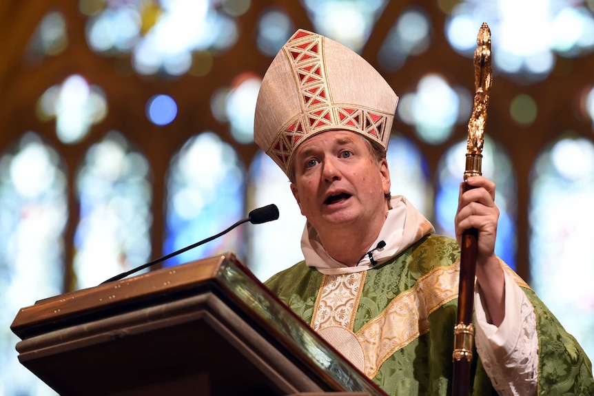 Fisher, decked out in clergy attire, presents a sermon.