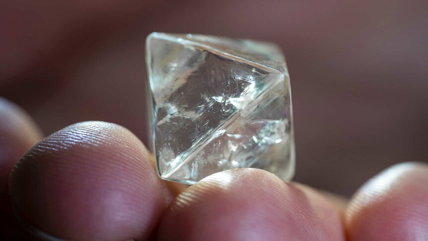 A close-up shot of a cube-shaped diamond in a person's hand.