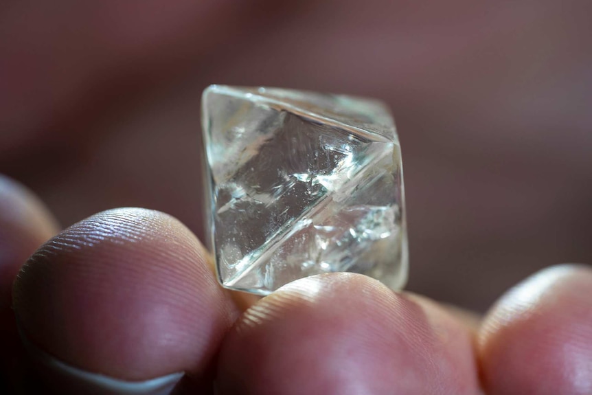 A close-up shot of a cube-shaped diamond in a person's hand.