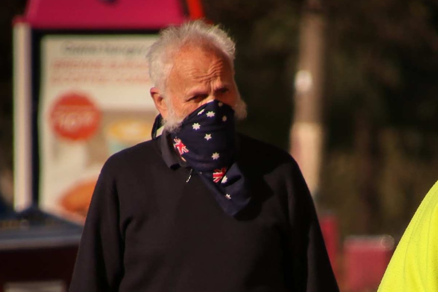 A man wearing a dark blue bandana over his mouth next to another man bending over, wearing a surgical mask.