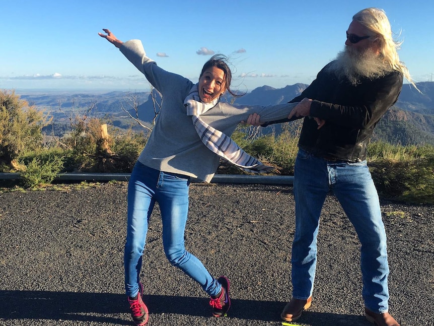 Bearded man holds woman by the arm on windy lookout