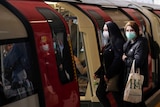 Two women wearing face masks step onto an underground train.