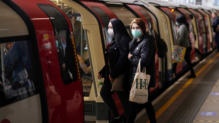 Two women wearing face masks step onto an underground train.