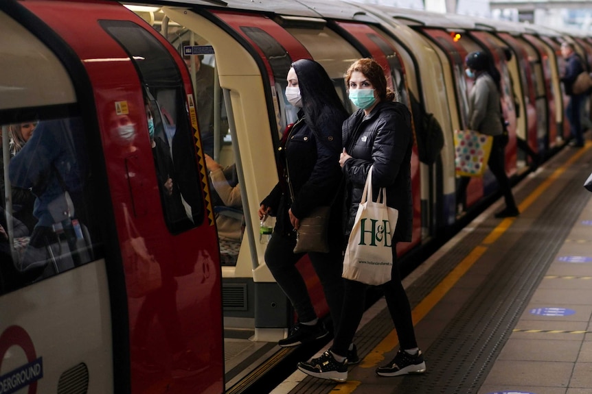 Two women wearing face masks step onto an underground train.