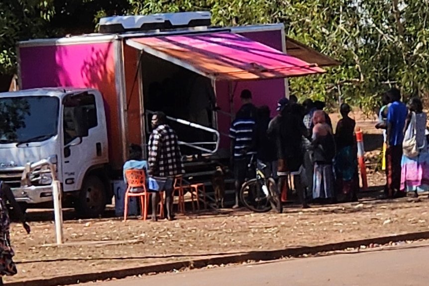 社区成员在北领地排队乘坐 Telstra 的一辆粉色巴士。