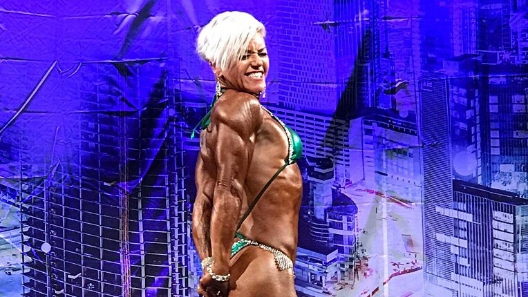 Female bodybuilder stands on stage smiling.