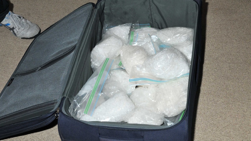 A suitcase lies opened on the ground with plastic bags stuffed with methylamphetamine inside.
