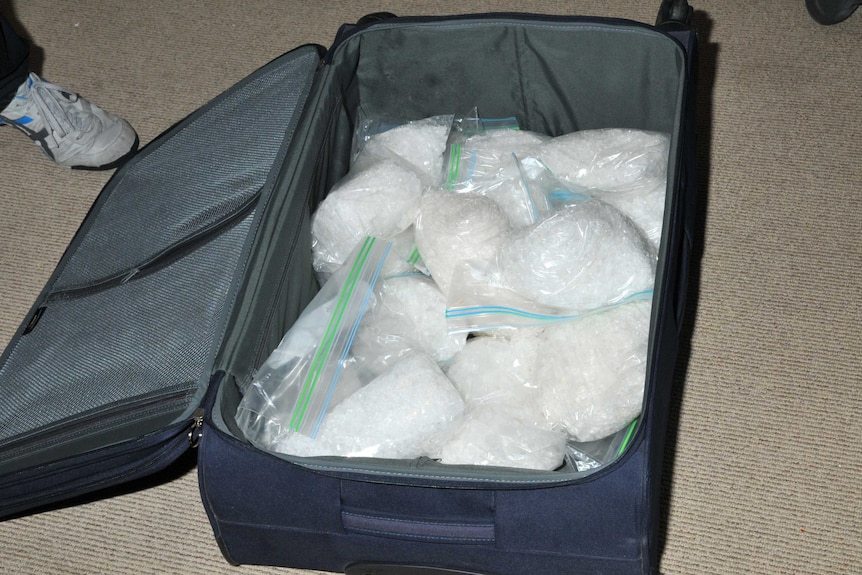 A suitcase lies opened on the ground with plastic bags stuffed with methylamphetamine inside.