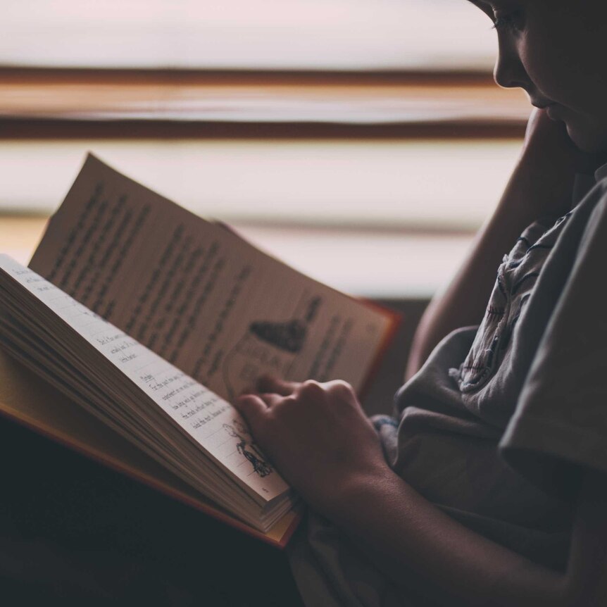 Young boy sits alone reading a book