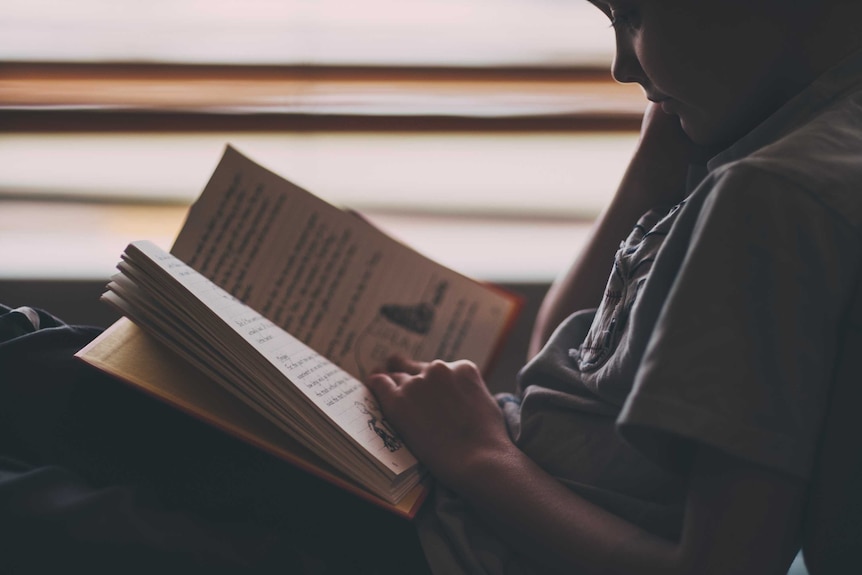 Young boy sits alone reading a book