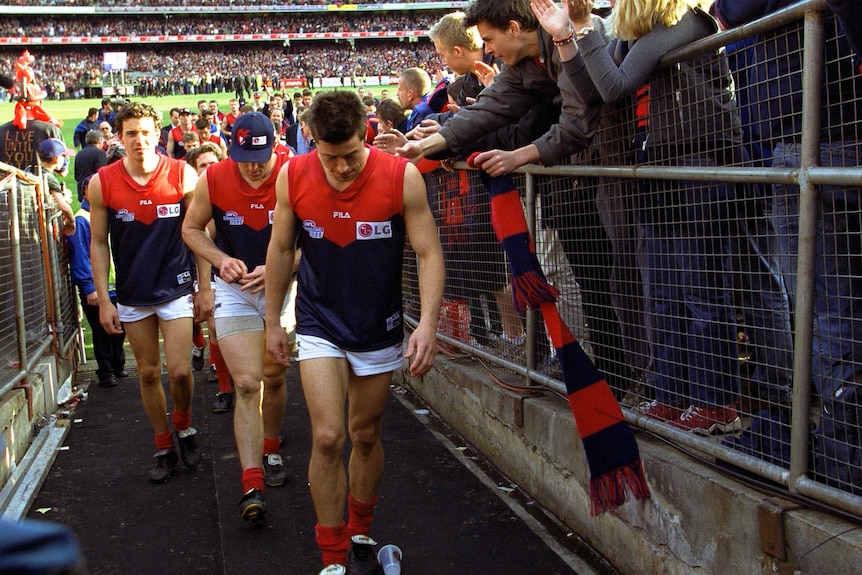 A group of Melbourne AFL players walk up the race with their heads down after losing a grand final as fans applaud