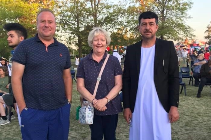 Three people stand in a park looking at the camera