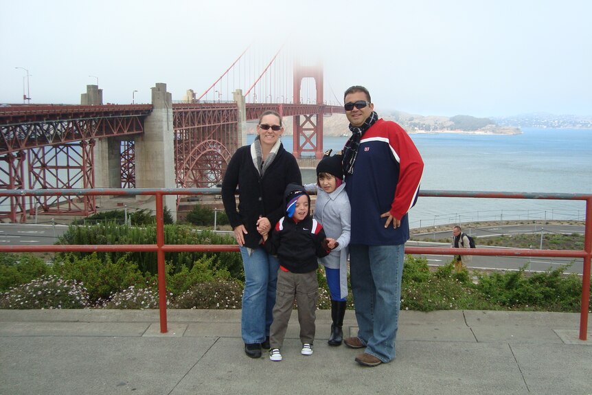 A family of four - mum, dad , son and daughter - smiling at the foggy Golden Gate Bridge. 