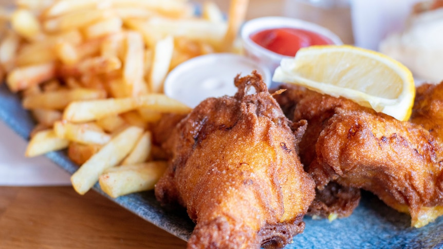 A plate of fish and chips with a wedge of lemon, sauce and mayo.