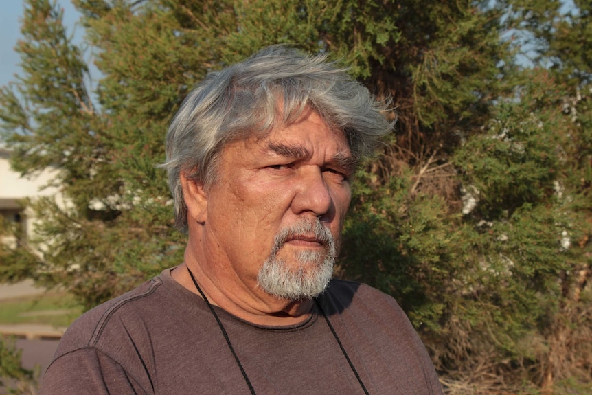 A man with grey hair and dark t-shirt squints at the camera.