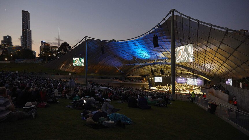The Melbourne Symphony Orchestra on stage at the Sidney Myer Music Bowl in semi-darkness as the sun has almost set.