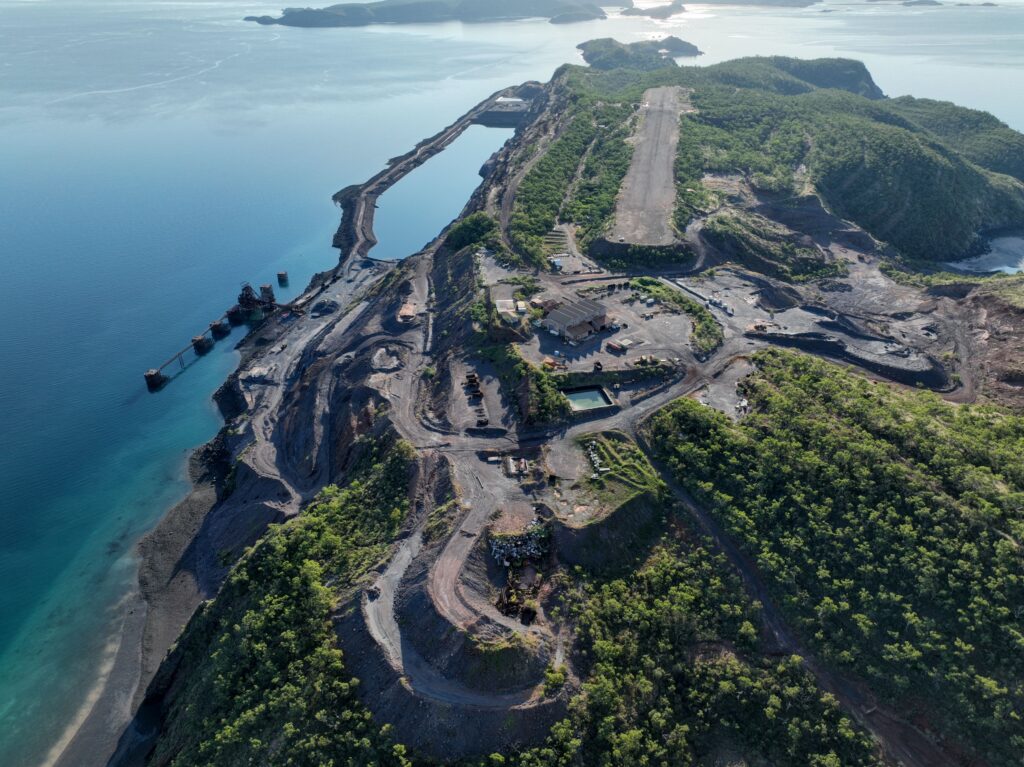 A view from the air of an island with dirt airstrip, small port and industry