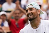 Australian tennis player Nick Kyrgios tugs at his shirt while smiling on court after winning at Wimbledon.
