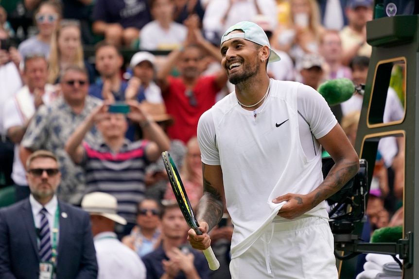 Australian tennis player Nick Kyrgios tugs at his shirt while smiling on court after winning at Wimbledon.