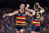 Two AFL players go to give each other a hug after a goal is kicked.
