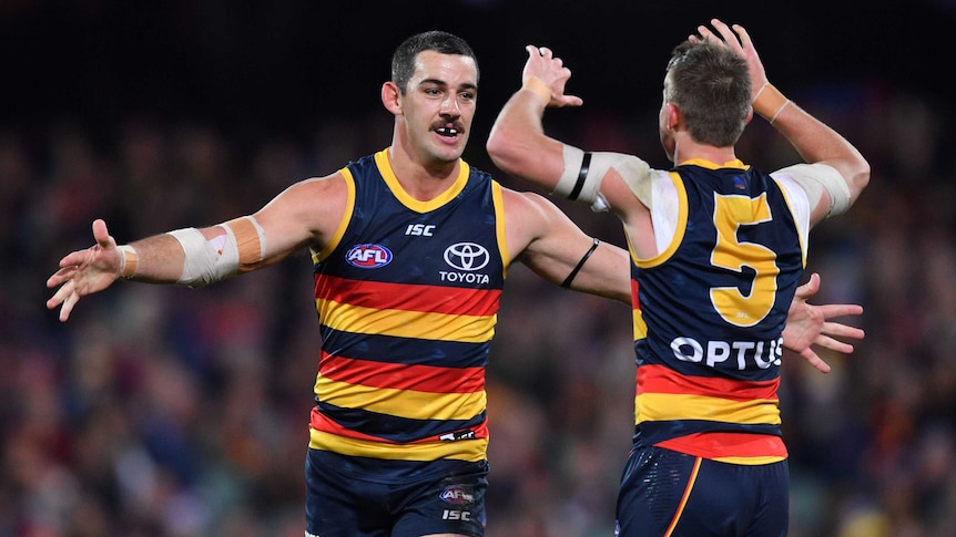 Two AFL players go to give each other a hug after a goal is kicked.