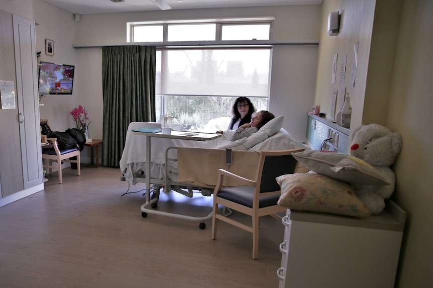 Angelina Giorgio lies in a hospital bed, Tania Giorgio sits beside her.