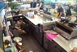 A worker crouching down in the kitchen as guests stand up and leave.