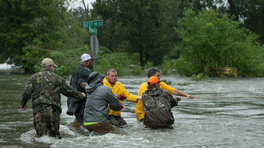 A group of men pull on a rope in waist-deep water.