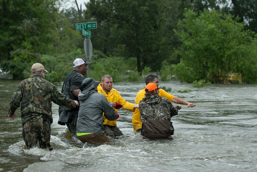 A group of men pull on a rope in waist-deep water.