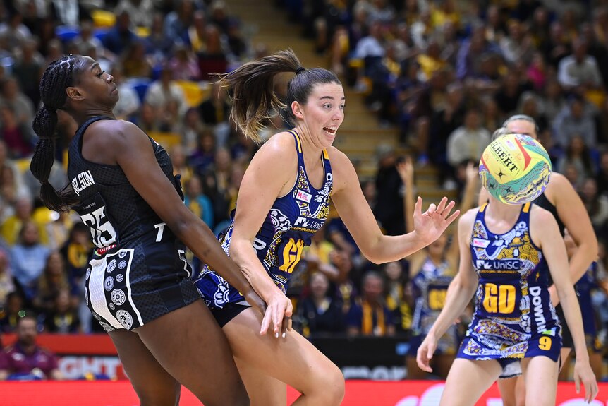 A Collingwood Magpies Super Netball player defends as a Sunshine Coast Lightning opponent chases the ball.
