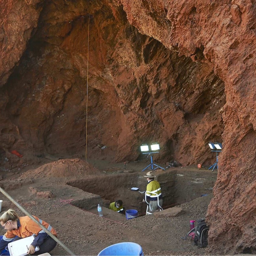 A group of archaeologists dig inside the Juukan-2 caves with lights set up around them.