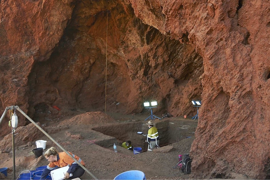 A group of archaeologists dig inside the Juukan-2 caves with lights set up around them.