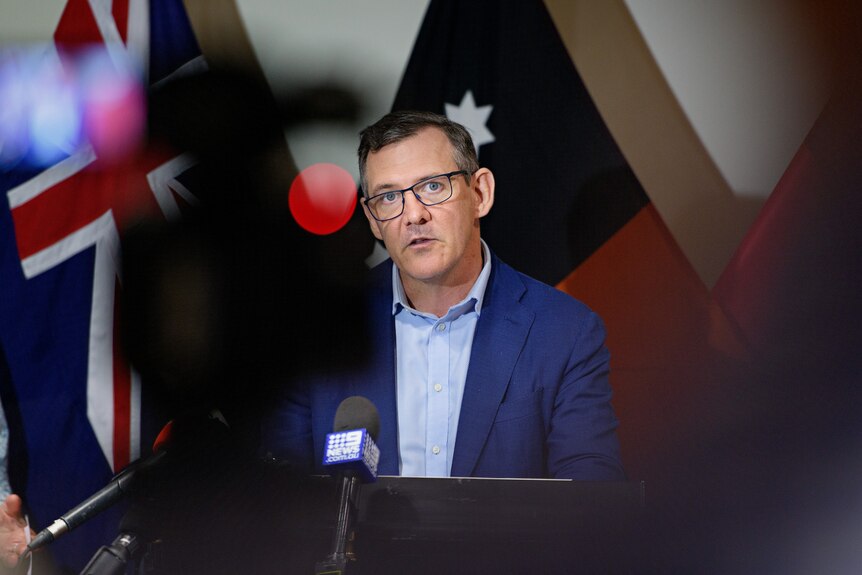 NT Chief Minister Michael Gunner stands in front of some flags, addressing the media.
