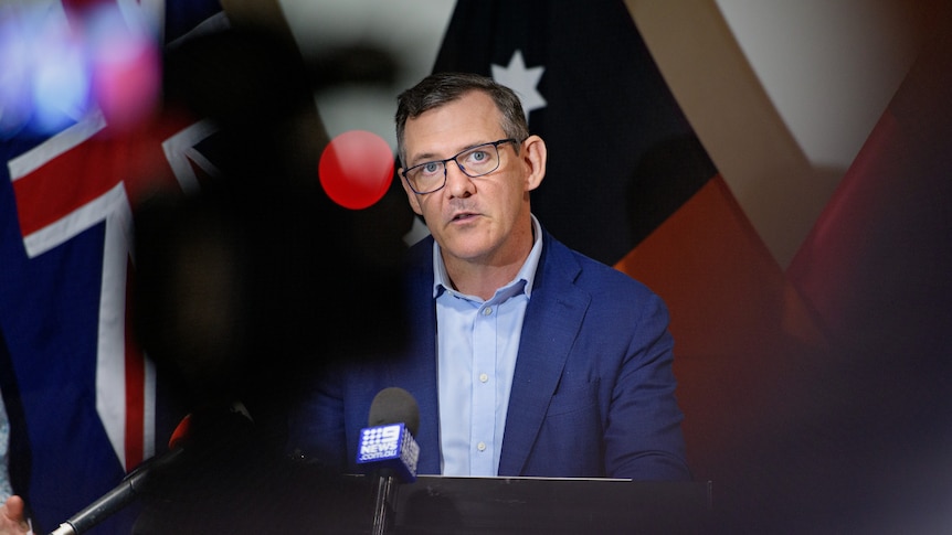 NT Chief Minister Michael Gunner stands in front of some flags, addressing the media.