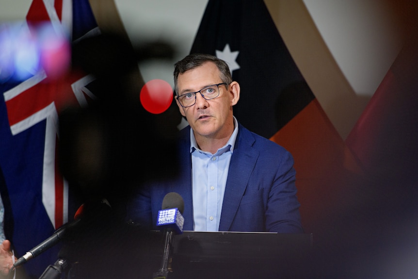 NT Chief Minister Michael Gunner stands in front of some flags, addressing the media.