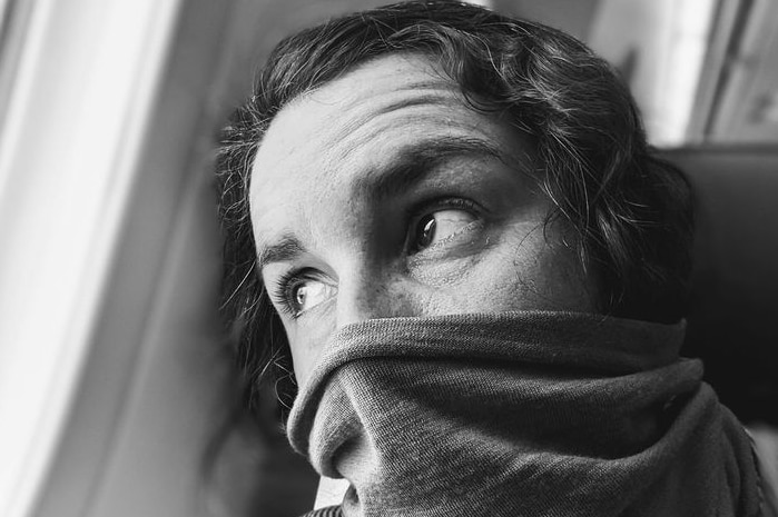 Woman wearing face covering looks out window