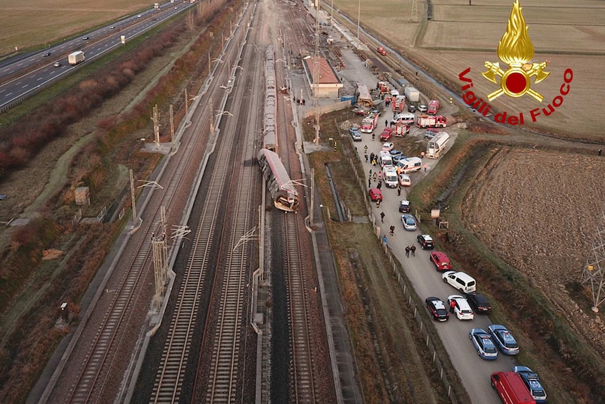 An aerial photo show a train derailed with cars and other vehicles stopped near by.